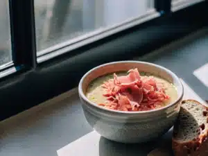 Cremige Erbsensuppe mit gezupftem Schinken, Brot und Butter in einer Schale