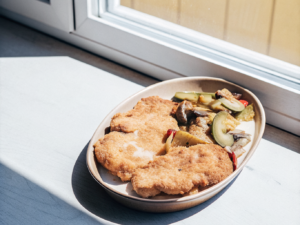 Ofenschnitzel mit cremiger Sauce, Paprika, Champignons und Gewürzgurken auf einem Teller