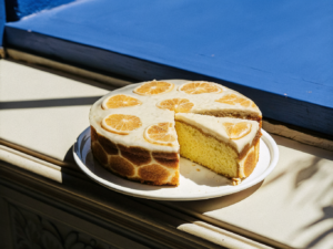 Mandarinen-Schmand-Kuchen mit glänzendem Fruchtbelag und einem angeschnittenen Stück auf einem weißen Teller