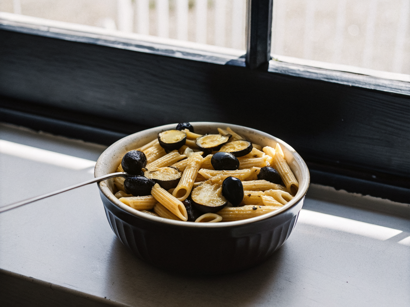 One-Pot-Pasta mit Zucchini und schwarzen Oliven 1 Penne mit Zucchini und schwarzen Oliven in Tomatensauce, angerichtet in einer flachen Schale