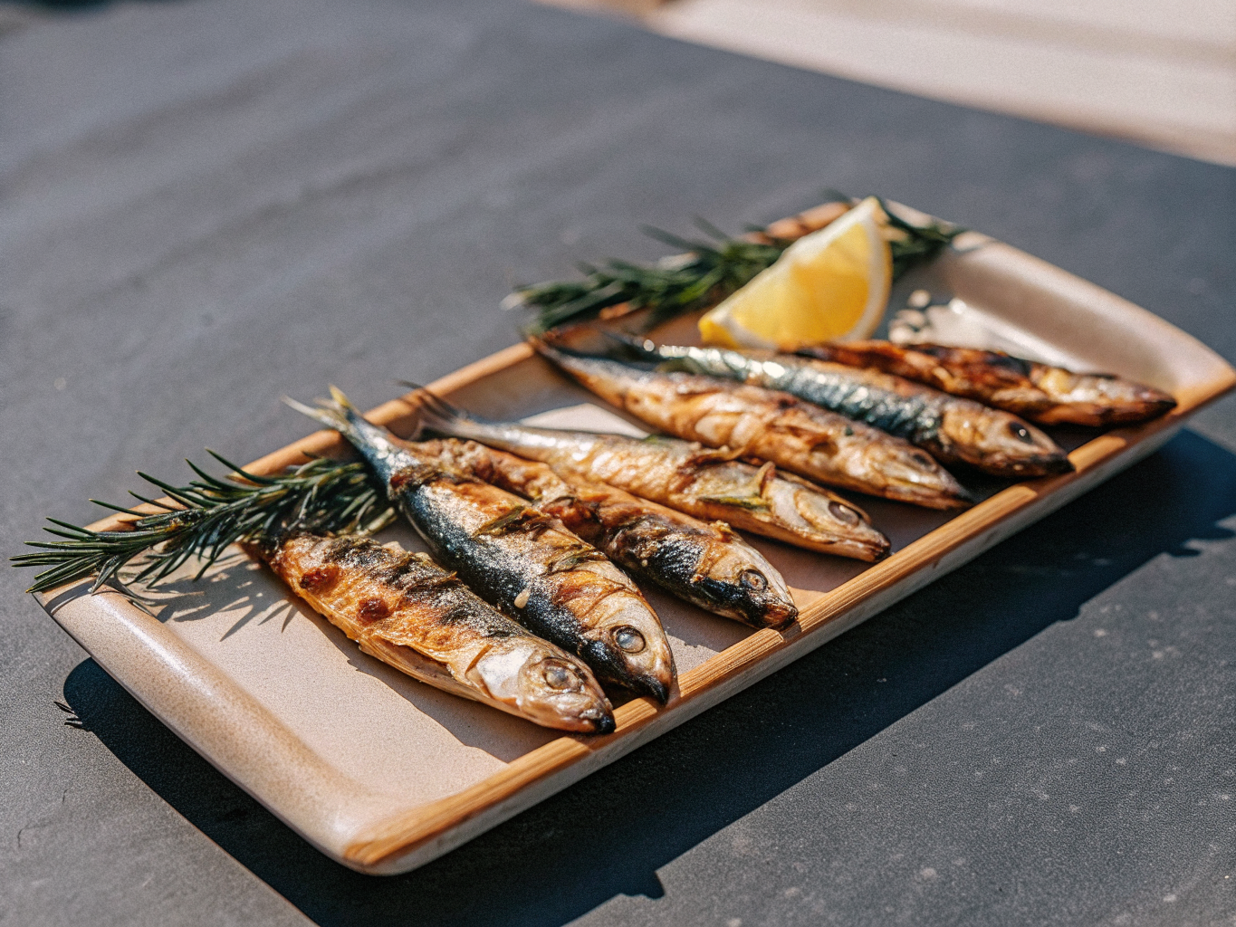 Gegrillte Sardinen mit Zitronenspalten und Rosmarin auf einer Servierplatte