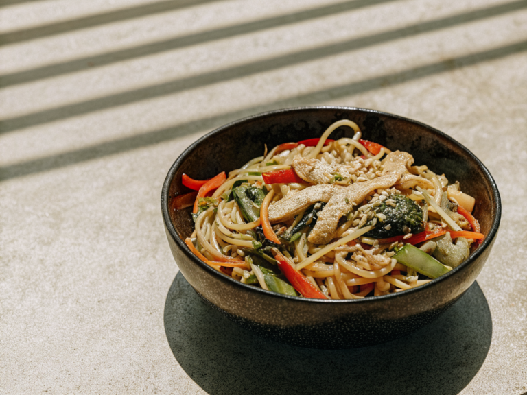 Wok-Bratnudeln mit Hähnchen, Paprika, Karotten und Brokkoli in einer Schale