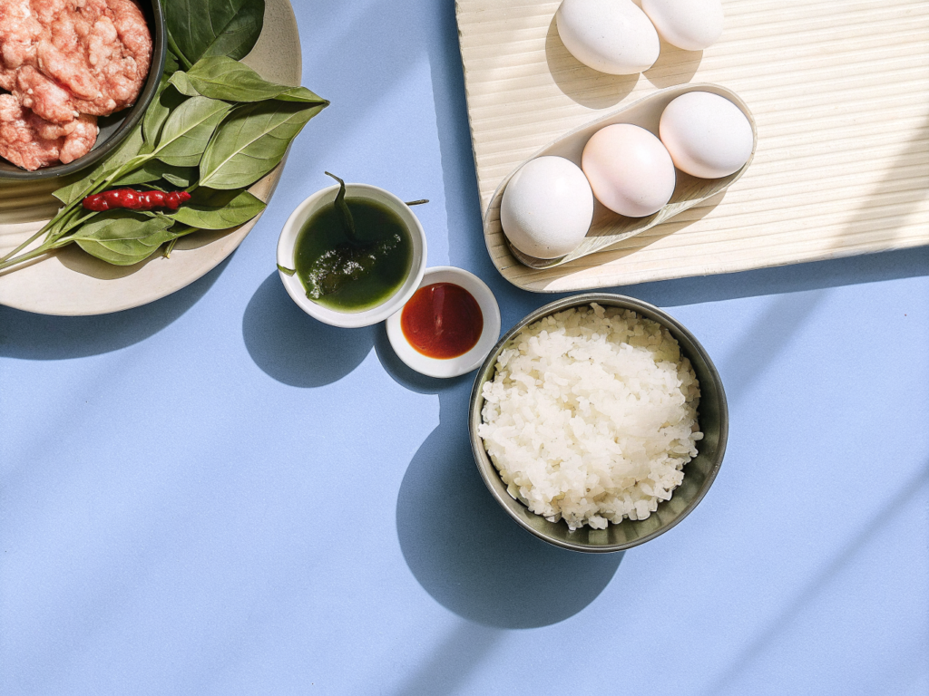 Pad Kra Pao aus dem Wok mit Schweinehack 2 Zutaten für Pad Kra Pao auf der Arbeitsfläche neben einem Wok
