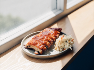 Zarte BBQ-Spareribs mit glänzender Sauce auf einem Teller, daneben Krautsalat