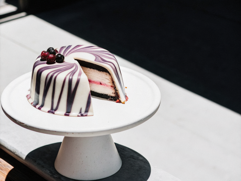 Glänzende Torte mit rosa-lila Glasur, Beeren und sichtbaren Schokoladen-, Mousse- und Fruchtschichten