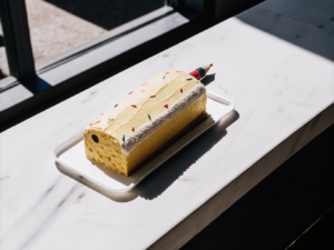 Buntstift-Torte mit gelber Creme, bunten Fondantbuchstaben und Streuseln auf einer weißen Platte