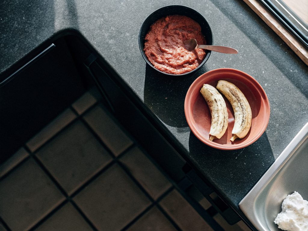Kochbananen-Kokos-Muffins ohne Mehl 2 Kochbananen, Kokoscreme und Zucker neben einer Schüssel mit zerdrückten Kochbananen